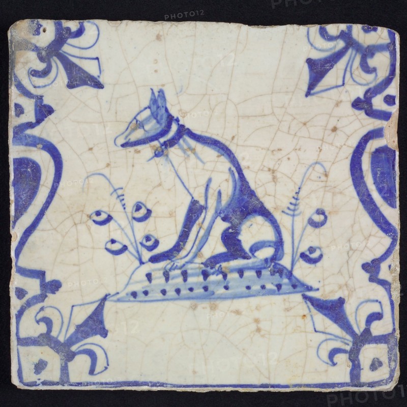 Animal tile, sitting dog to the left on plot between balusters, in blue on white, corner pattern French lily, wall tile