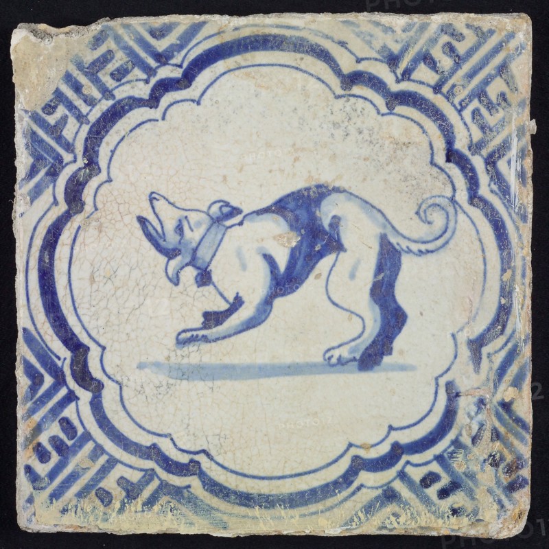 Animal tile, barking dog to the left inside scalloped frame with braces, in blue on white, corner motif meanders, wall tile