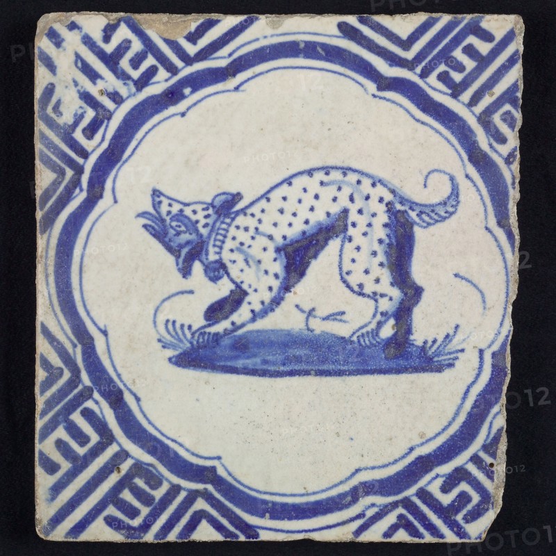 Animal tile, barking dotted dog to the left on plot within scalloped frame, in blue on white, corner pattern meanders, wall tile