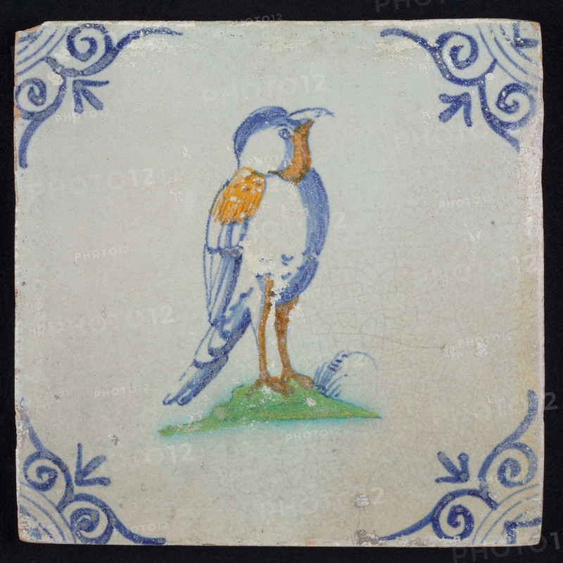 Animal tile, bird with on ground to the right in orange, yellow, green and blue on white, corner pattern ox head, wall tile