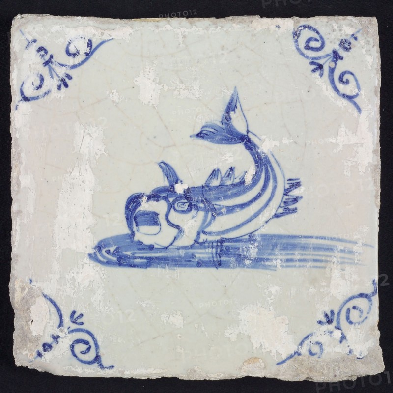 Animal tile, unknown fish in water to the left with open beak and curled tail, in blue on white, corner motif steered ox's head