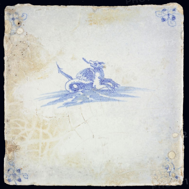 Sea creature tile, in blue on white, dragon-like creature with wings and pintail in water to the right, corner pattern spider