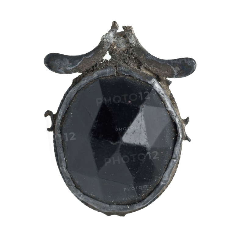 Black, oval cut stone, encased in metal frame, jewelery clothing accessory clothing fragment soil find silver? stone glass metal