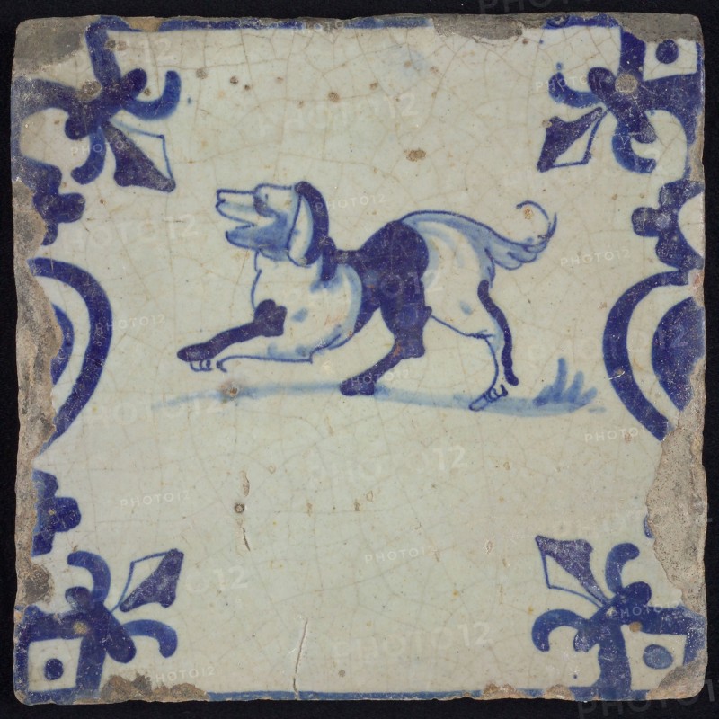 Animal tile, jumping dog to the left on plot between balusters, in blue on white, corner pattern French lily, wall tile
