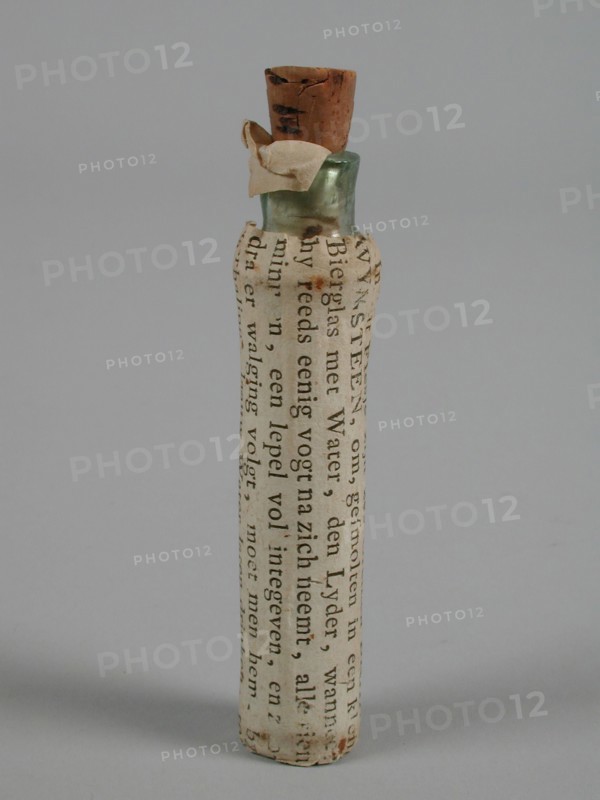 Transparent glass bottle with vomit and label In this bottle are six Greinen BRAAKWYNSTEEN, bottle holder medicine pharmacy