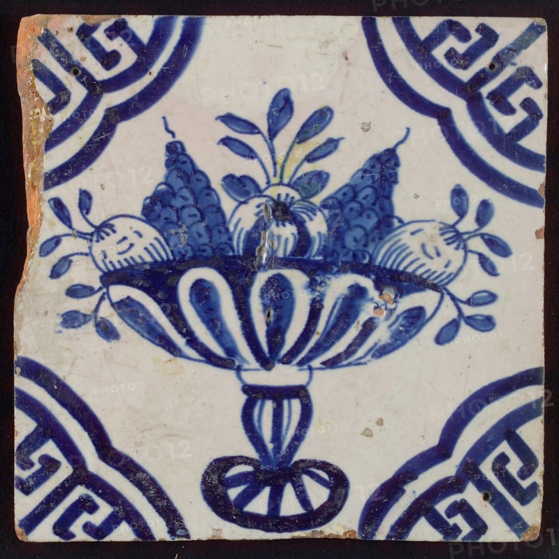 White tile with blue fruit bowl on stand, apples and grapes; corner pattern meander angle, wall tile tile sculpture ceramic