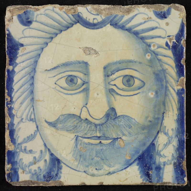 Tile of chimney pilaster, blue on white, head of man with long curly hair and mustache, beginning of shell-shaped headdress