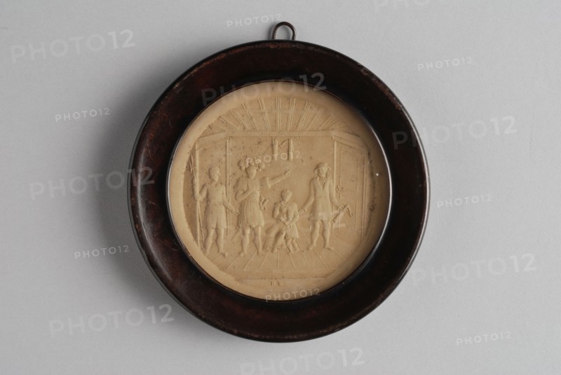 Small circular relief plaque in wooden frame, with historical representation of four people and child in room, plaque embossed