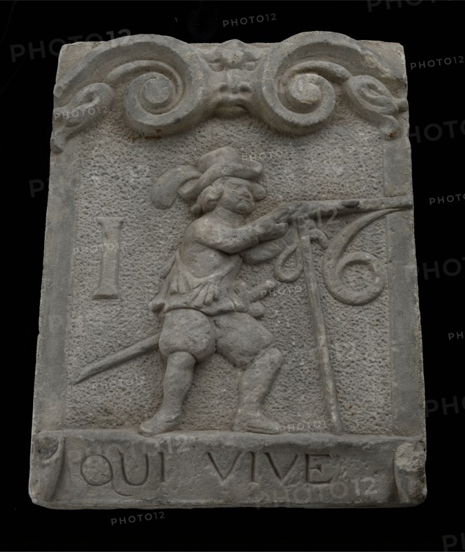 Wall brick from gate with musketeer and ribbon with text qui vive 16, facing stone sculpture sculpture building component