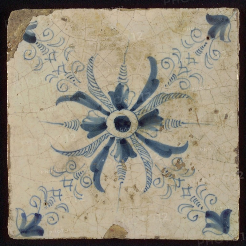 Ornament tile, blue on white, central dot, around which stylized flower shape ending in two diagonals, clocks, wall tile