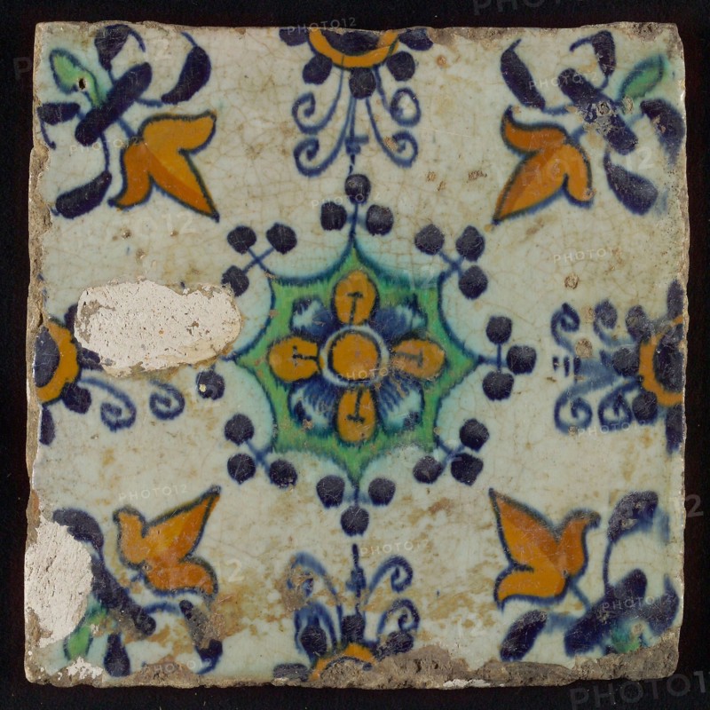 Tile, blue draft, yellow, green and orange on white, central flower within star shape, three-spot around, half rosette, corner