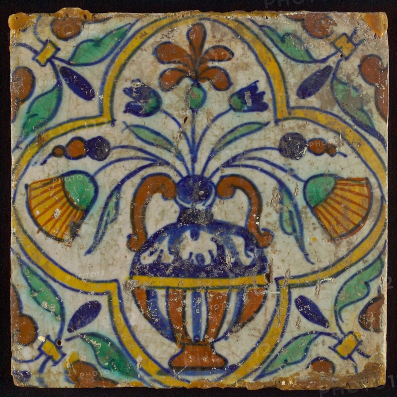 Tile, blue draft, yellow, orange, brown and green on white, centrally flower pot within four-sided frame, corner motif, wall