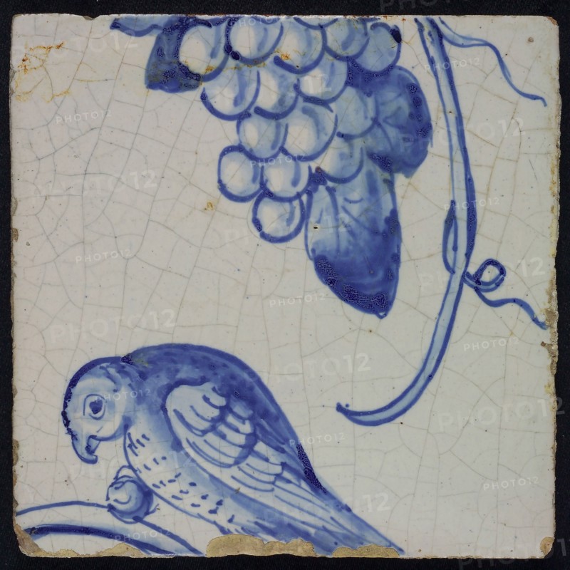 Blue tile with bird in left side view, sitting on branch with grape between the paw, grape bunch and tendril of pilaster with 39