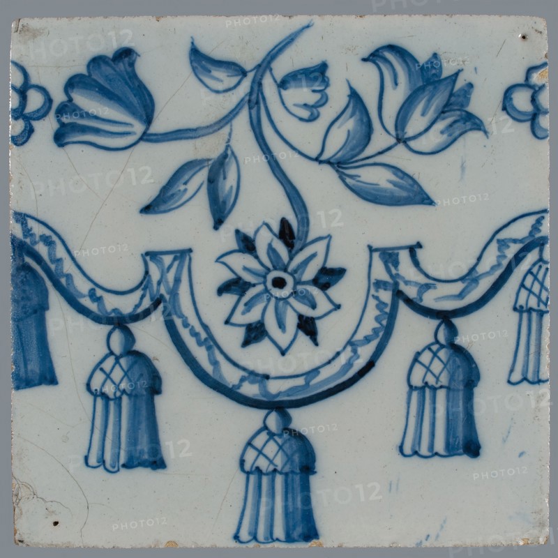 Border tile, blue on white, garland with tassels, above which flower tendril with two tulips and other flower, vertically