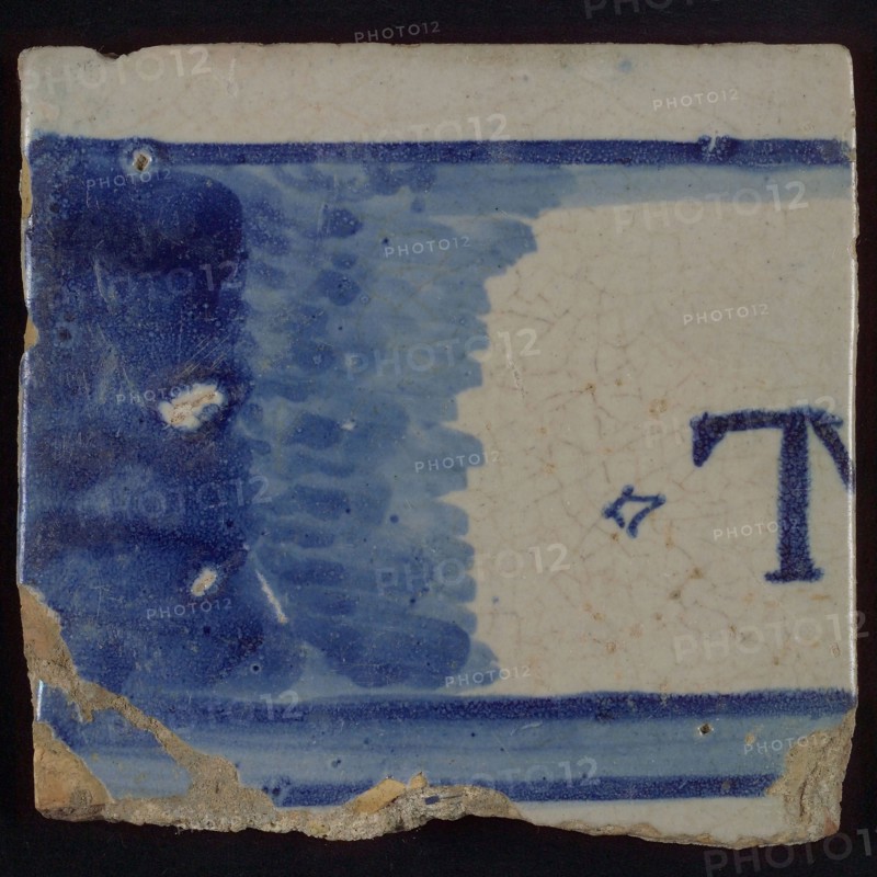 White tile with horizontal surface, partly blue colored, in which letter T, tile picture footage fragment ceramics pottery glaze