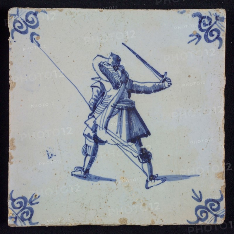 White tile with blue warrior with plume hat, spear and raised sword, seen from behind; corner pattern ox head, wall tile