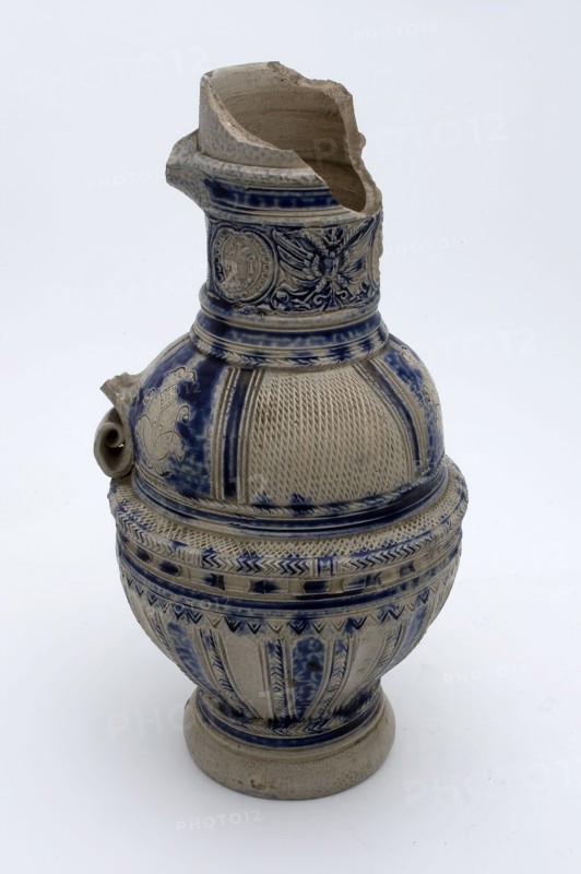 Stoneware jug with kerf-cut decor on shoulder, round neck band with three medallions in which mask, jug crockery holder soil