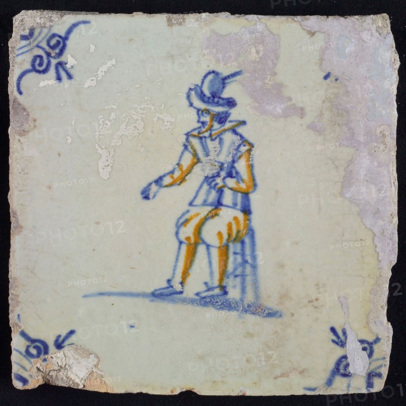 White tile with yellow and blue soldier on stool, ox-head corner motif, wall tile tile sculpture ceramics pottery glaze, baked