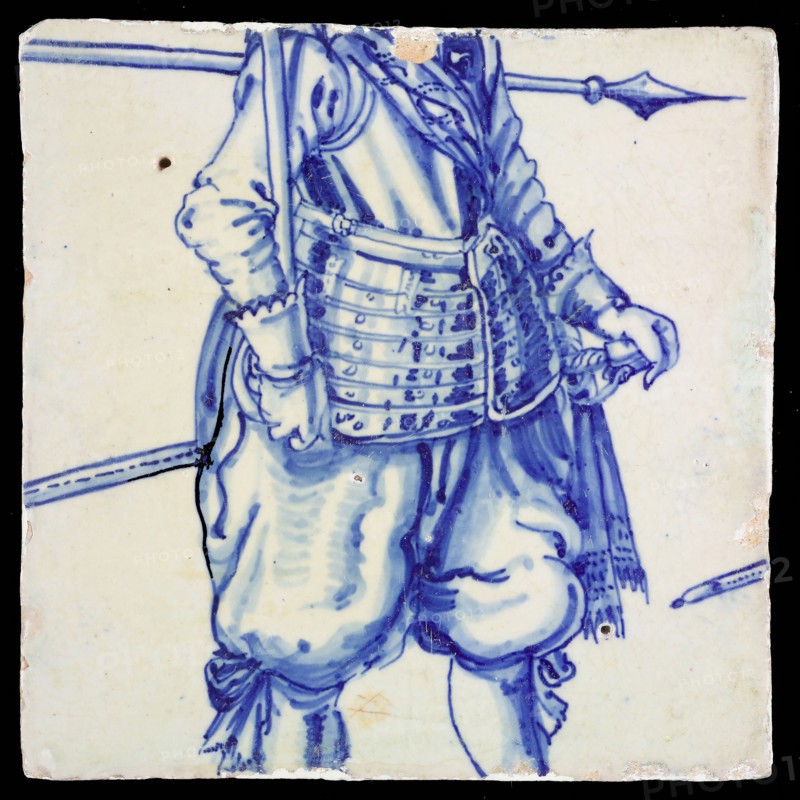 Tile, in blue on white, below an ornamental border, above it two lower legs of soldier with shoes and bows, tile picture footage
