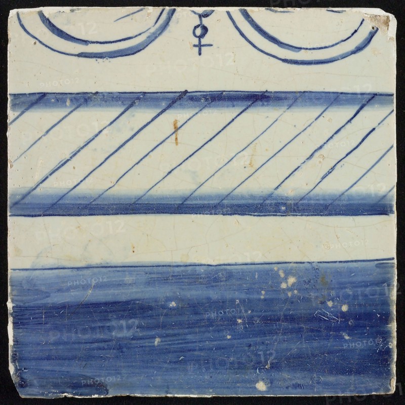 Tile, blue on white, border with filled part and part with hatching, top edge visible part of bow and ball with cross, tile