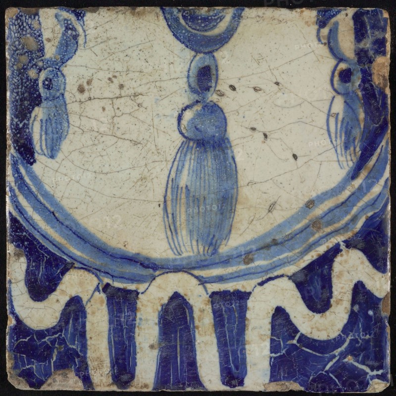 Tile of chimney pilaster, blue on white, bottom of pleated lap with three hanging tassels underneath and garland edge, chimney