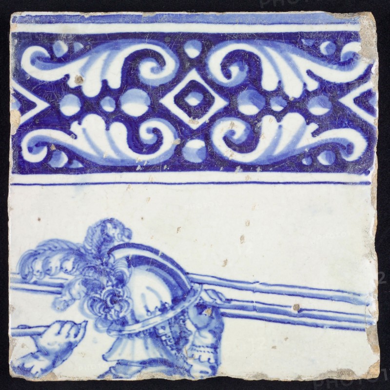 Tile, in blue on white, above ornament edge, underneath the head of soldier with helmet and plume, the hand of another soldier