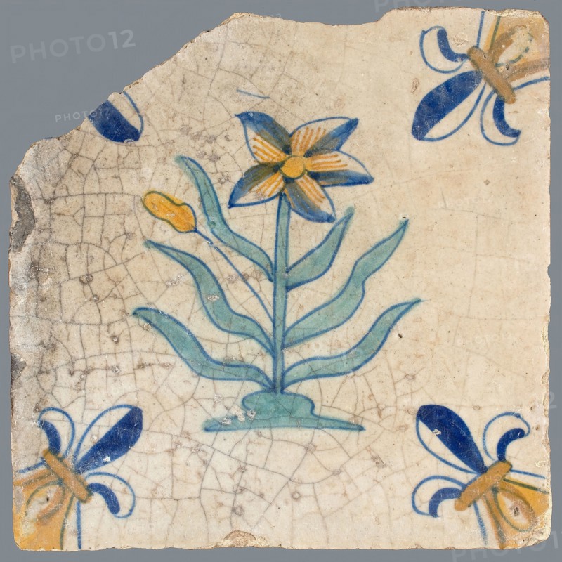 Tile, flower on ground in yellow, brown, green and blue on white, corner pattern french lily, corner point yellow, wall tile