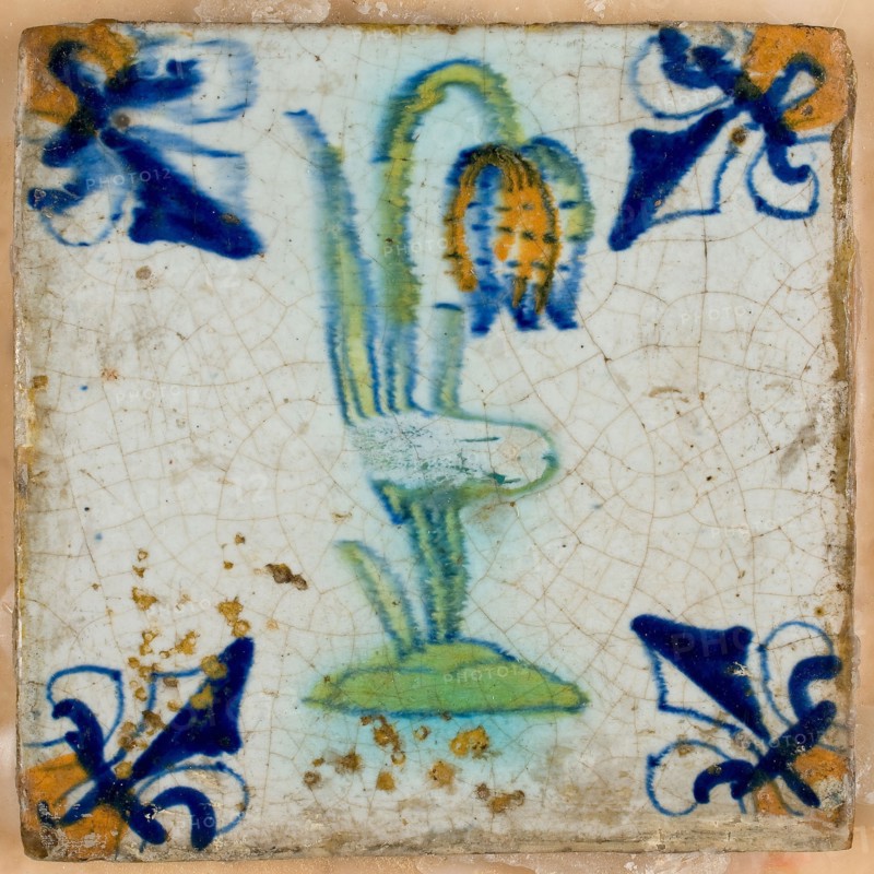 Tile, flower on ground in orange, green and blue on white, corner pattern french lily, corner point orange, on shelf in wax