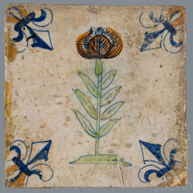 Tile, flower on ground in orange, green and blue on white, corner pattern french lily, corner point orange, wall tile