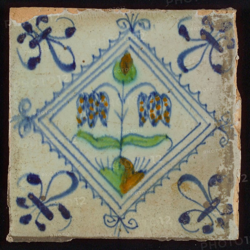 Tile, double flower on ground in orange, green and blue on white, inside serrated square with plume, corner pattern french lily
