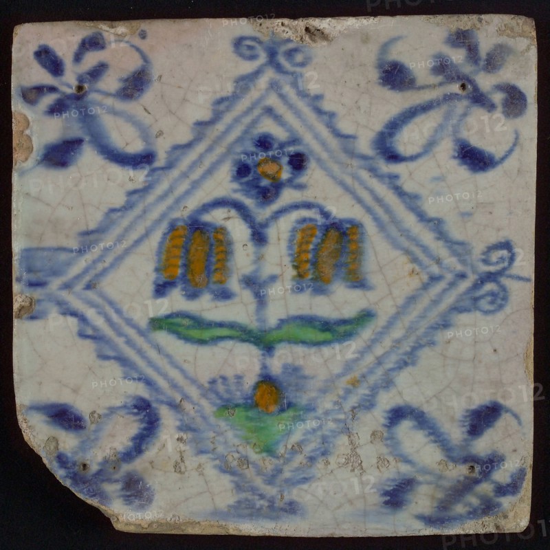 Tile, double flower on ground in orange, green and blue on white, inside serrated square with plume, corner pattern french lily