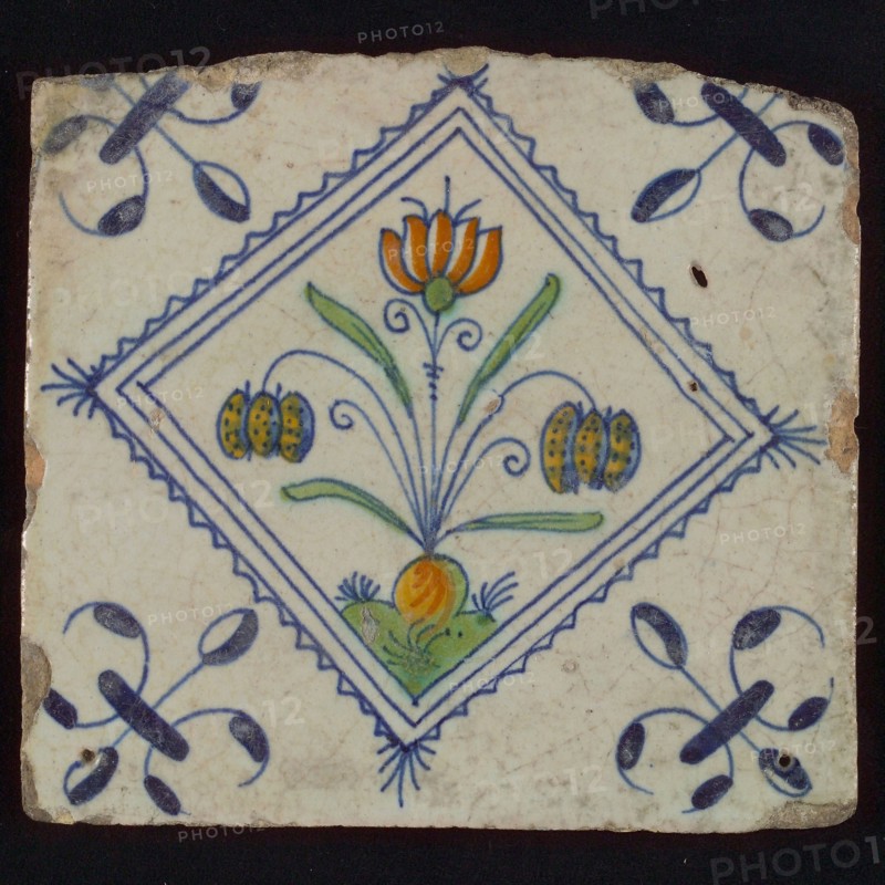 Tile, double flower on ground in orange, green and blue on white, inside serrated square with plume, corner pattern french lily