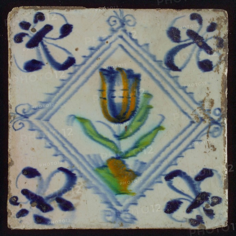 Tile, tulip on ground in orange, green and blue on white, inside serrated square with plume, corner pattern french lily, wall