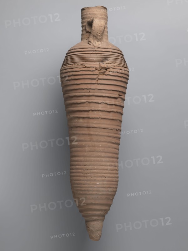 Amphora, unknown Egyptian workshop; amphorae, Egyptian amphoras, Egyptian ceramics, storage vessels, Coptic vessels, amphoras, amphoras; Nile clay; inscribed amphoras, inscribed vessels. Wine transport vessel with a strongly elongated belly, narrowed in the middle. Roller-shaped vices, approximately oval in cross-section, are glued to the central section of the neck with a straight rim. These connect to the upper section of the convex, steep shoulders. The base is conical and conically terminated. The entire surface of the vessel, brown and even, is covered with grooves of varying density and profile. The interior was impregnated with a black resinous substance, streaks of which are visible in the upper part of the neck. The clay is brown, alluvial Naqlun AC1A ceramic body type. On the upper part of the arms, between the vices, is an inscription in red paint: ICX. On the lower part of the arms, below the inscription, is a hollowed-out hole with a diameter of approximately 0.5 cm. 2nd h...
