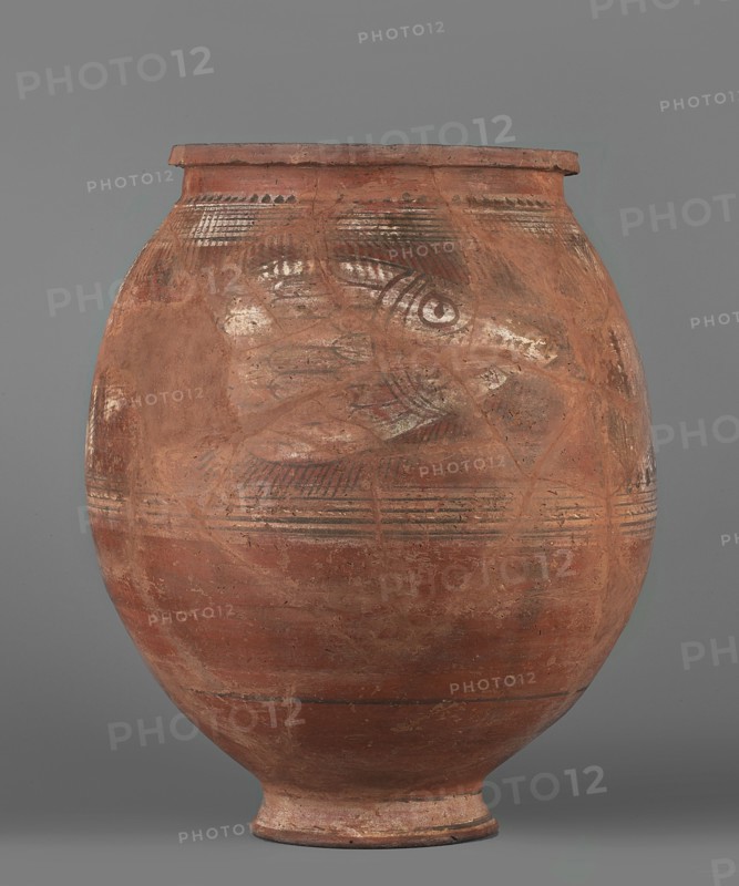 Pithos, unknown Egyptian workshop. Storage vessel with an ovoid belly, small annular high foot, and rim with a vertically beveled edge slightly protruding outward. At the point of greatest diameter there is an imprint of the rope used to tie the vessel during drying. Decoration only on the upper part of the belly: on both sides an image of a fish with a short body wider toward the tail—body and tail in side view, head viewed from above with visible eyes separated by a horizontal row of dots; fins rendered with lines. Fish bodies painted white with black contour and detail lines; each fish is flanked top and bottom by wide white lines with thin black lines painted on each. The fish are separated by a vertically painted braid on a white background, framed by black lines, with short diagonal lines terminating in dots. Painted Coptic storage vessel, figural, floral, and impressed decorative elements. 6th–7th century, Edfu. Vessel; height 43.8 cm, width 34.1 cm., A large rounded pottery ves...