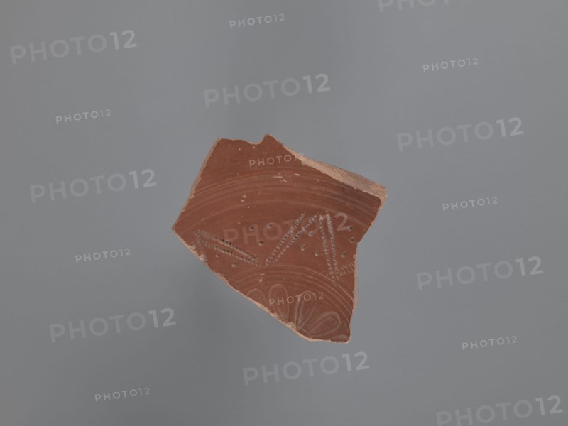 Plate fragment, unknown Aswan workshop site type / place of origin, plates, tableware, Aswan pottery, Egyptian pottery, Egyptian sigillata, Coptic vessels, Coptic pottery, impressed decorations, stamped decorations, stamps, kaolin clay. Fragment of the bottom of a plate with a ring-shaped foot. Pink kaolin ceramic mass Gempeler 1A. The surfaces are polished and covered with a reddish-brown engobe. The vessel is decorated internally, on the bottom of the bowl, using pressing and engraving techniques. These create a composition whose central element is a rosette impressed with almond-shaped stamps forming a pattern. It is surrounded by five concentrically engraved grooves. The band surrounding them consists of a double-course zigzag, made with an impressed roulette. The fields between the zigzag arms are filled with rhomboidal impressions of a stylus . The entire composition is enclosed by eight concentrically engraved grooves. 5th–6th century, unknown type of site / place of discovery, ...