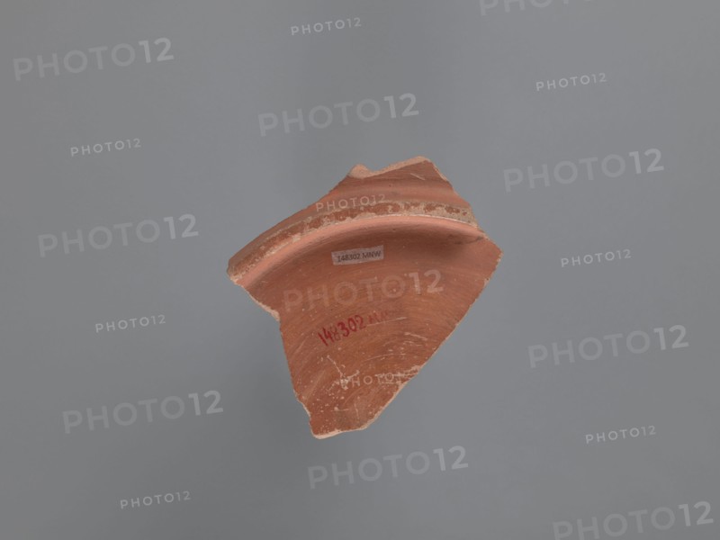 Plate fragment, unknown Aswan workshop, plates, tableware, Aswan pottery, Egyptian pottery, Egyptian sigillata, Coptic vessels, Coptic pottery, impressed decorations, stamped decorations, stamps, kaolin clay. Fragment of the bottom of a plate with a ring-shaped foot. Pink kaolin ceramic mass Gempeler 1A. The surfaces are polished and covered with a reddish-brown engobe. The vessel is decorated internally, on the bottom of the bowl, using pressing and engraving techniques. These create a composition whose central element is a rosette impressed with almond-shaped stamps forming a pattern. It is surrounded by five concentrically engraved grooves. The band surrounding them consists of a double-course zigzag, made with an impressed roulette. The fields between the zigzag arms are filled with rhomboidal impressions of a stylus . The entire composition is enclosed by eight concentrically engraved grooves. 5th–6th century, vessel, plate, height 2.7 cm, width 11.4 cm, diameter 10 cm bottom, A b...