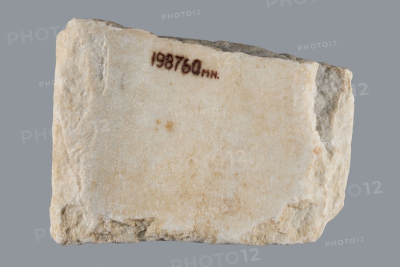 Euphemia's Epitaph, Greek inscriptions, tombstone epitaph. Preserved central fragment of a white marble slab; top and bottom chipped, inscription intact. In the center a large cross with almost equal arms widening at the ends; the inscription is placed between the arms. Rounded letters placed between marked thin lines; letter height 1.5–2.1 cm, average line spacing 0.2 cm. Origin: Bithynia or Constantinople, 6th–7th century, Asia Minor. Stele; height 15.0 cm, width 20.5 cm, depth 3.2 cm., A roughly rectangular slab with a rough, uneven surface and broken edges, showing a pale off-white to beige stone with areas of light tan and small darker spots, set against a solid gray background.