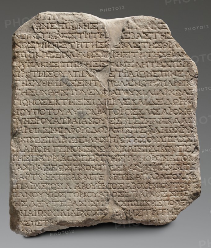 Honorific inscription, unknown workshop of Asia Minor author, repossession, Roman legions, military decorations, 120–130, Asia Minor Heraclea Salbake, inscription; height 57 cm, width 49 cm, depth 8 cm, weight 49.5 kg, A roughly rectangular stone slab with an irregular top and chipped edges, showing a weathered, uneven surface and a vertical crack near the center; the slab is light beige to pale gray with darker gray shadowing in recessed areas, and there are subtle warm tan and brown patches on parts of the surface; the face of the slab is covered by a grid-like pattern of shallow carved horizontal lines and repeated short carved marks within those lines, creating a textured, incised appearance; overall the stone sits against a smooth neutral gray background.