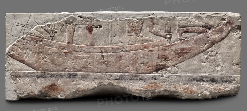Fragments of wall decoration from the mastaba of the dignitary Tepemankh; Niuserre ruler of Egypt; ca. 2445–2421 BC, Tepemankh ca. 2445–2421 BC., Iconography: sacrificial artists, scribes, mastabas, shipwright; scenes of boat building and bringing funerary offerings. Egyptian, sepulchral funerary architecture; Scen.Gal.Eg., Egyptian architecture. Date: c. 2445–c. 2421 BC, Old Kingdom, 5th Dynasty Nyuserre's reign. Place of origin: Abusir. Medium: bas-relief. Dimensions: height 26 cm, width 302 cm, depth 16 cm; weight 140 kg., A carved stone relief showing a long boat shape with a curved prow and stern, shallow hull details, and the suggestion of people through carved arms and hands holding poles; the surface has worn carved lines and shallow incisions outlining the boat and figures. The stone shows a palette of pale off-white and beige with areas of reddish-brown pigment on the boat and some brownish spots and smudges across the surface, plus darker grayish marks along a lower band. Th...