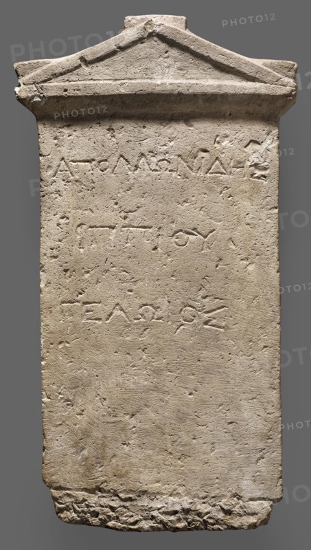 Tombstone of Apollonides with Greek inscription. Rectangular slab with three lines of Greek inscription, topped with a triangular tympanum. Tombstone of Apollonides, son of Hippias of Gela, 300–250 BC; Ptolemaic period. Found at Zawiyet el-Mayetin near Minia, Kom el Ahmar. Greek inscription. Height 58.5 cm, width 32 cm, depth 9 cm, weight 25.5 kg., A tall rectangular stone slab with a triangular pediment at the top, showing a rough, weathered surface and chisel marks; the stone is mostly beige and light tan with areas of darker brown discoloration and small patches of off-white; the top edge has a raised triangular molding and some chipped and uneven edges, the sides are straight but worn, and the bottom edge is irregular and broken with a jagged texture; the face of the slab has shallow, incised grooves and a few shallow depressions and scratches across its surface, giving it a pitted appearance; overall the slab appears solid and aged with a muted palette of beige, tan, brown, and of...