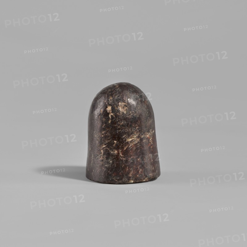 Grinder, Grinder in the shape of a rounded cylinder with a flat base, 2nd century, from Edfu, tool, height 2.8 cm, A rounded, dome-shaped object with a smooth, slightly irregular surface sits on a flat surface; the object shows a dark brown to nearly black base color with lighter brown, tan, and muted reddish patches and streaks across its surface, and it casts a soft shadow to one side against a uniform light gray background.