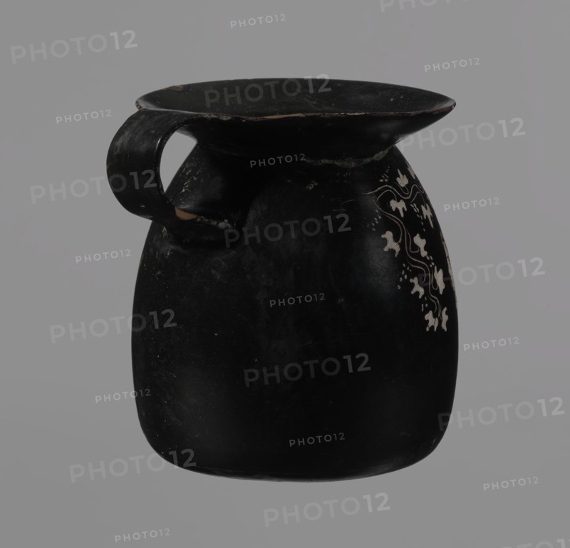Gnathia-style mug, antique vessel, mug; Gnathia style Southern Italy, Apulia; 4th–3rd century BC. Red clay with glossy varnish, white-painted decoration and yellow retouching. Flat bottom, convex belly tapering at the top into a wide spout; band-like lip. Decoration mainly opposite the lip on the upper belly: three elongated female heads turned left, shown in profile with large eyes and hairstyles shaded with yellow, surrounded by an ornament of ivy fruit and leaves. Vessel/cup., A dark rounded ceramic vessel with a wide flat rim and a single curved handle is shown against a gray background; the vessel is primarily black with a slightly worn surface and small areas of lighter wear, and one side features a decorative pattern of pale, cream-colored floral shapes and flowing lines.