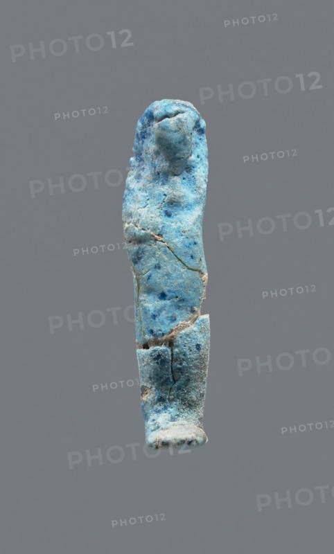 Shabti, mummy-shaped figurine, funerary gift. Legs missing. Arms crossed on the chest. Hands invisible under the shroud. Smooth tripartite wig. Facial details invisible. Not inscribed. 664–332 BC Late Period, Egypt. Height 3.7 cm., A small upright figurine-like object with a rough, weathered surface in shades of bright blue, pale blue, and turquoise with scattered darker blue spots, showing visible cracks and chips; the top is rounded and slightly bulbous, the middle tapers and then widens toward the lower section, and the base is flatter and more irregular, all set against a solid grey background.