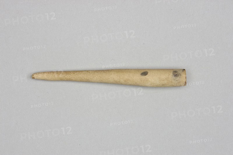 Mosaic cone, mosaic cones, decorative elements, Sumer, Near Eastern architecture, Eastern Gallic Scenography, 4th millennium BC; Uruk culture, Sumer, Southern Mesopotamia, element of architectural decoration, unknown creator/author., A single elongated tapered object lies horizontally against a neutral flat background, showing a cylindrical thicker end that narrows to a rounded tip; the object is mostly beige with areas of darker brown discoloration and small dark spots, and the background appears light gray.