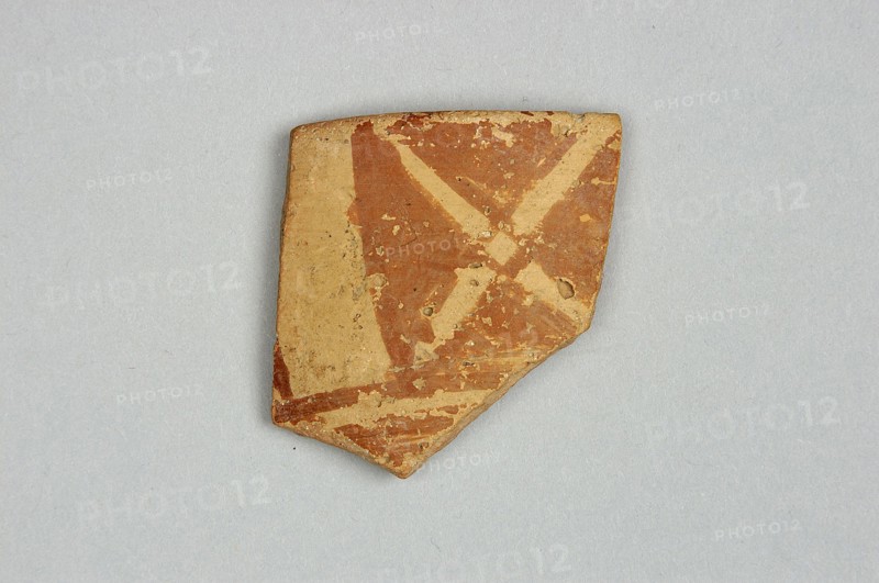 Fragment of a bowl spout, 6th millennium BC, Northern Mesopotamia, vessel, A broken piece of pottery with a triangular outline sits on a light gray background, showing a surface of reddish-brown and beige with chipped and worn areas, a few rough edges, and patches of lighter beige where the top layer has flaked away.