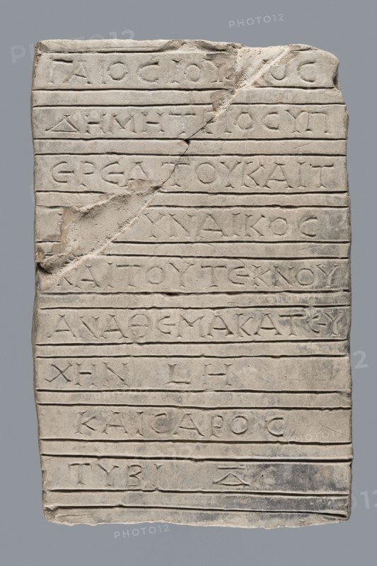 Greek inscription of thanksgiving, tombstone inscription, 30.12.23 BC, Egypt, Greek inscription, height 24.0 cm, width 14.0 cm, depth 5.8 cm, A rectangular pale stone slab with a rough, uneven surface and carved horizontal grooves across its width, showing a diagonal chip and break near the upper middle left and a few small undulations along the edges; the slab is primarily light gray to off-white with subtle darker gray smudges and areas of shadow, and the carved recesses appear slightly darker than the surrounding stone.