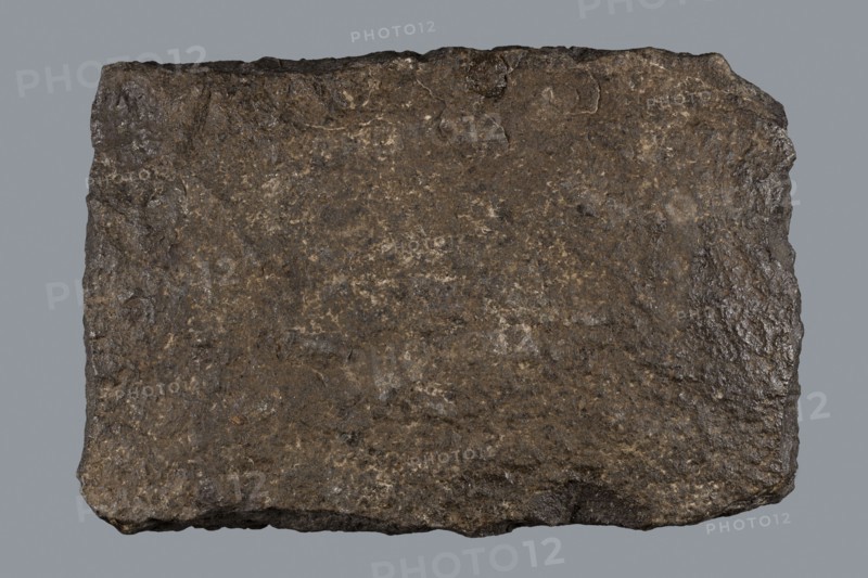 Greek dedicatory inscription, tombstone inscription, 2nd half of the 2nd century BC, Egypt, Greek inscription; height 22.0 cm, width 32.5 cm, depth 7.0 cm, A roughly rectangular, flat slab with an uneven, textured surface in shades of brown, dark brown, gray, and hints of tan, showing rough, chipped edges and a varied granular pattern across its face, set against a uniform gray background.
