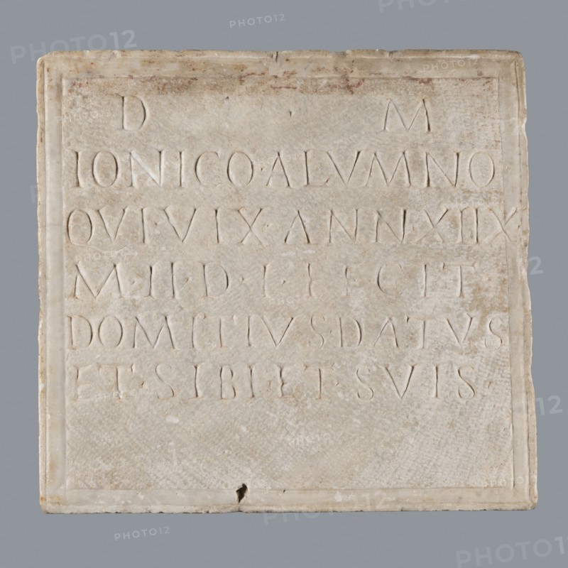 Latin grave inscription, unknown author, 2nd century, Roman Empire 27 BC–476, slab epitaph, grave inscription, height 31 cm, width 28 cm, A square pale beige stone plaque with a slightly raised border sits against a neutral gray background. The plaque surface shows a weathered, uneven texture with small chips and areas of darker beige and faint brown discoloration. There is a shallow rectangular recessed area within the border, and shallow carved grooves and lines are visible across the surface. The stone has lighter cream highlights and subtle off-white areas, and a small darker spot appears near the bottom edge. Overall the visible colors include beige, cream, off-white, gray, and faint brown.
