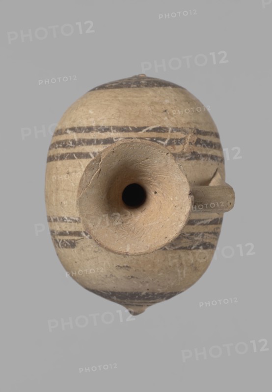 Cypriot gourd jug, Excavations at Nea Paphos Cyprus. Cypriot pottery, Cypriot Bichrome Ware III. Small vessel with a barrel-shaped gourd-shaped body, without a foot, with a spherical bottom. On both shorter sides the center is marked with a small protruding point. A single ring-shaped handle on the longer side, mounted above half the height of the body and to the base of the neck, curved downwards. Quite long neck, strongly flaring, conical spout. Yellow clay with yellow-brownish engobe. Decoration in black-brown and matte red: the spout is decorated externally with a wide matte red band beneath which is a narrower black band; the belly is decorated on both sides with two groups of three concentric black-and-brown lines of varying widths and spacing, with the outer line in the groups on the shorter sides much wider than the others. Protruding points are marked in black-and-brown. 850–700 BC, Cyprus, vessel., An oval ceramic vessel viewed from above with a rounded body and a central fun...